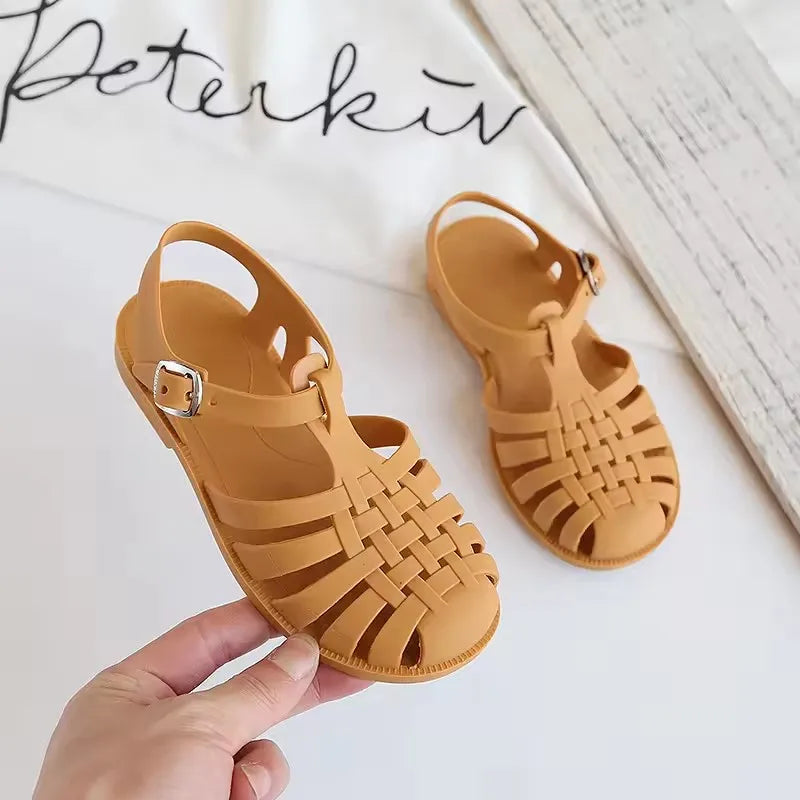 A pair of tan girls' gladiator jelly sandals with woven straps and a non-slip sole.