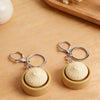 A pair of beige fidget keychains with round white tops resting on a wooden surface.