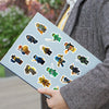 A hand holds a sheet of cartoon ninja stickers for kids against a blurred outdoor background.