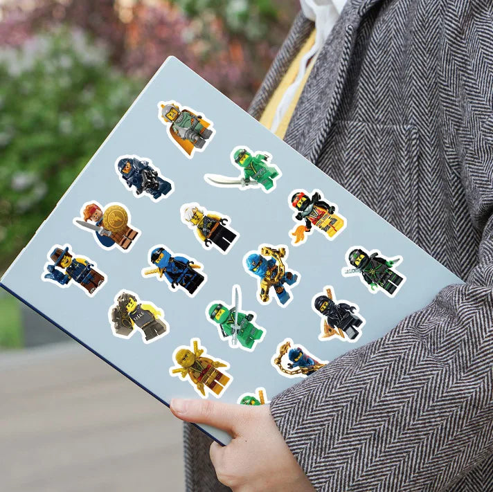 A hand holds a sheet of cartoon ninja stickers for kids against a blurred outdoor background.