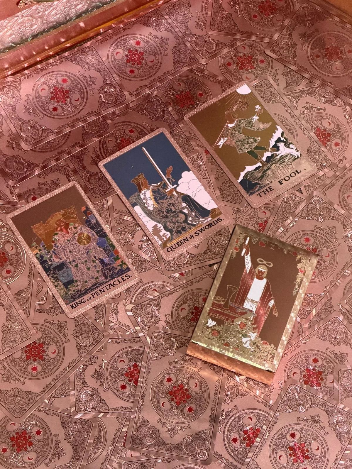 A collection of mini gold foil tarot cards, including the Fool, Queen of Swords, King of Pentacles, and other cards, displaye
