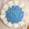 A white plate filled with numerous small, light blue plastic beads for crafting.