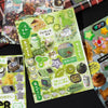 A sheet of decorative cut film stickers featuring cute animals and food items on a green background for scrapbooking