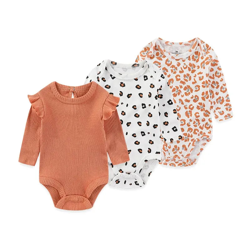 A set of three orange and white patterned cotton baby bodysuits with long sleeves
