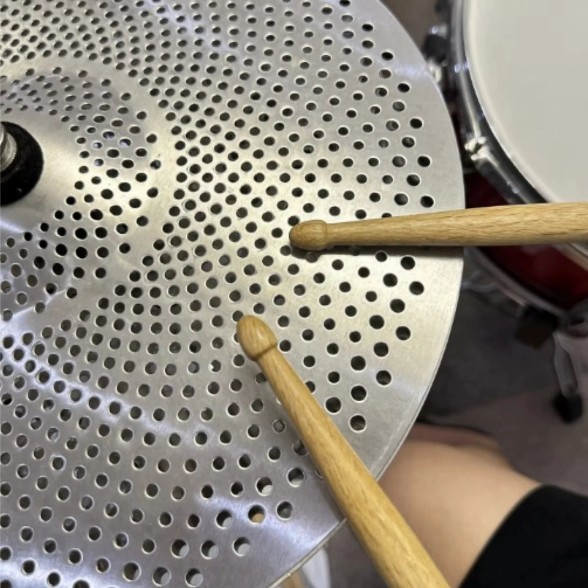 A pair of light wood maple drumsticks resting on a silver perforated practice pad.