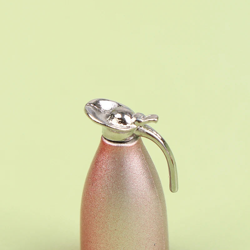 A miniature silver alloy kettle with a handle is shown against a pale green background.