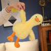 A yellow plush toy of a duck with orange feet is being held by a person against a blue background.