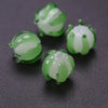 Several small, translucent green glass charms shaped like lily of the valley buds are displayed on a dark surface.