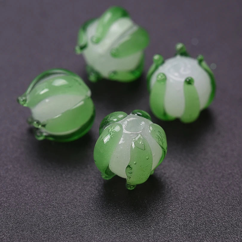 Several small, translucent green glass charms shaped like lily of the valley buds are displayed on a dark surface.