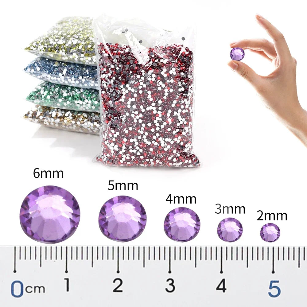 A clear bag of flat-back resin rhinestones in various shades of purple and pink, measured against a ruler.