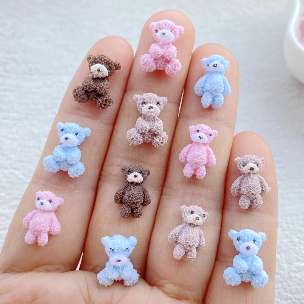 A hand displays various small, fuzzy resin teddy bear charms in shades of pink, purple, and blue.