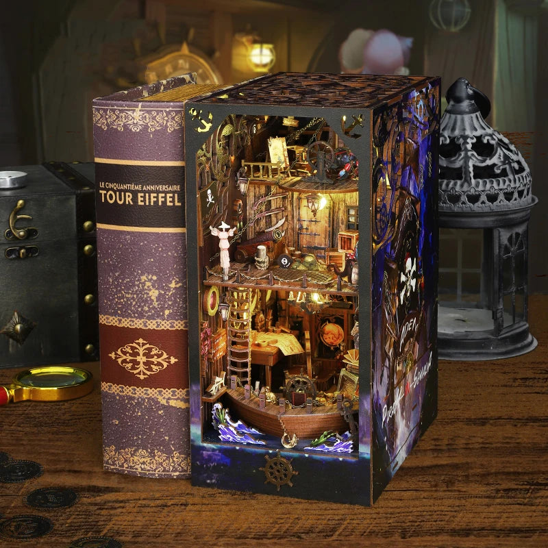 A wooden book nook kit featuring a detailed pirate ship scene inside a box with an Eiffel Tower themed book.
