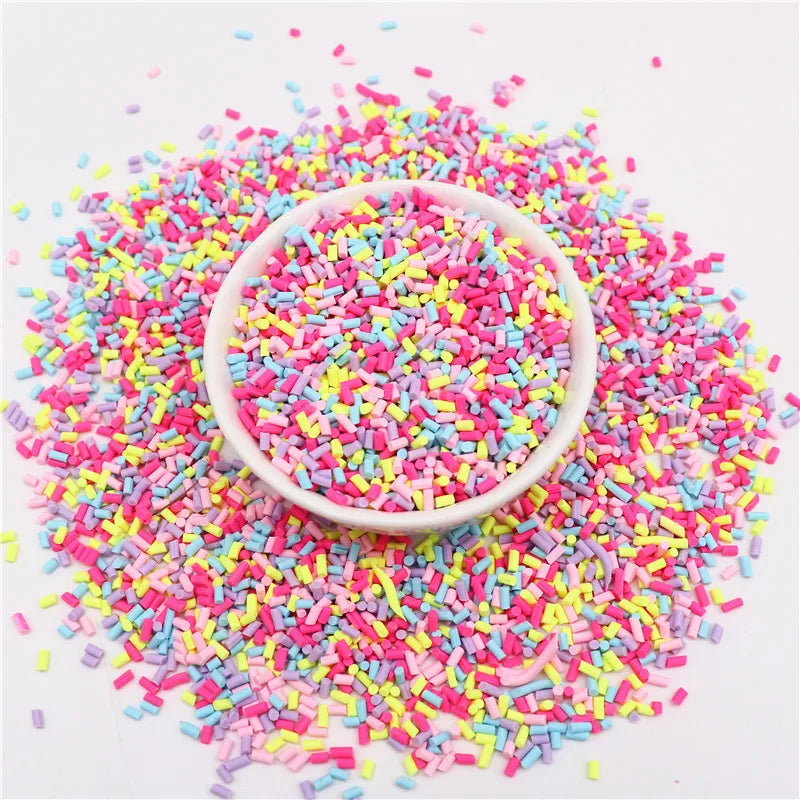 A pile of colorful polymer clay slice sprinkles in various shades of pink, blue, and yellow scattered on a white surface.