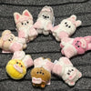A collection of pink and white cartoon animal plush keychains arranged in a circle on a dark gray fabric.