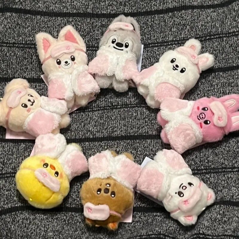 A collection of pink and white cartoon animal plush keychains arranged in a circle on a dark gray fabric.