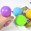 A hand holds a purple squishy stress ball next to various colored foam balls on a sheet of paper.
