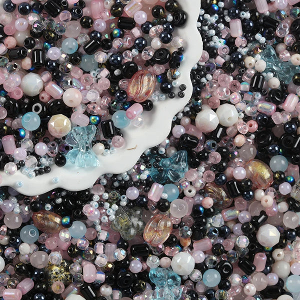 A close-up view of various colorful crystal glass spacer beads in pink, blue, and black shades scattered on a white surface.