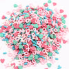 A pile of pink and teal polymer clay flower charms scattered on a white background.