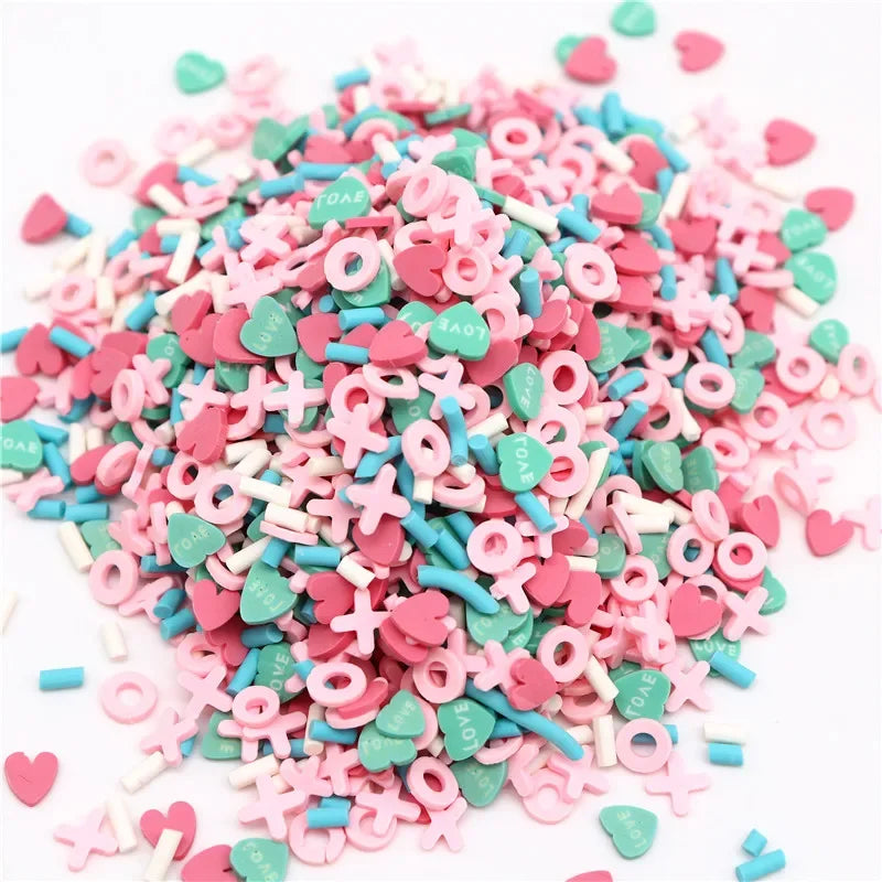 A pile of pink and teal polymer clay flower charms scattered on a white background.