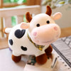 A soft, white and brown cow plush toy with a plaid collar sitting on a surface.