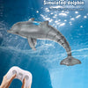 A simulated dolphin toy is shown swimming underwater, controlled by a white remote.