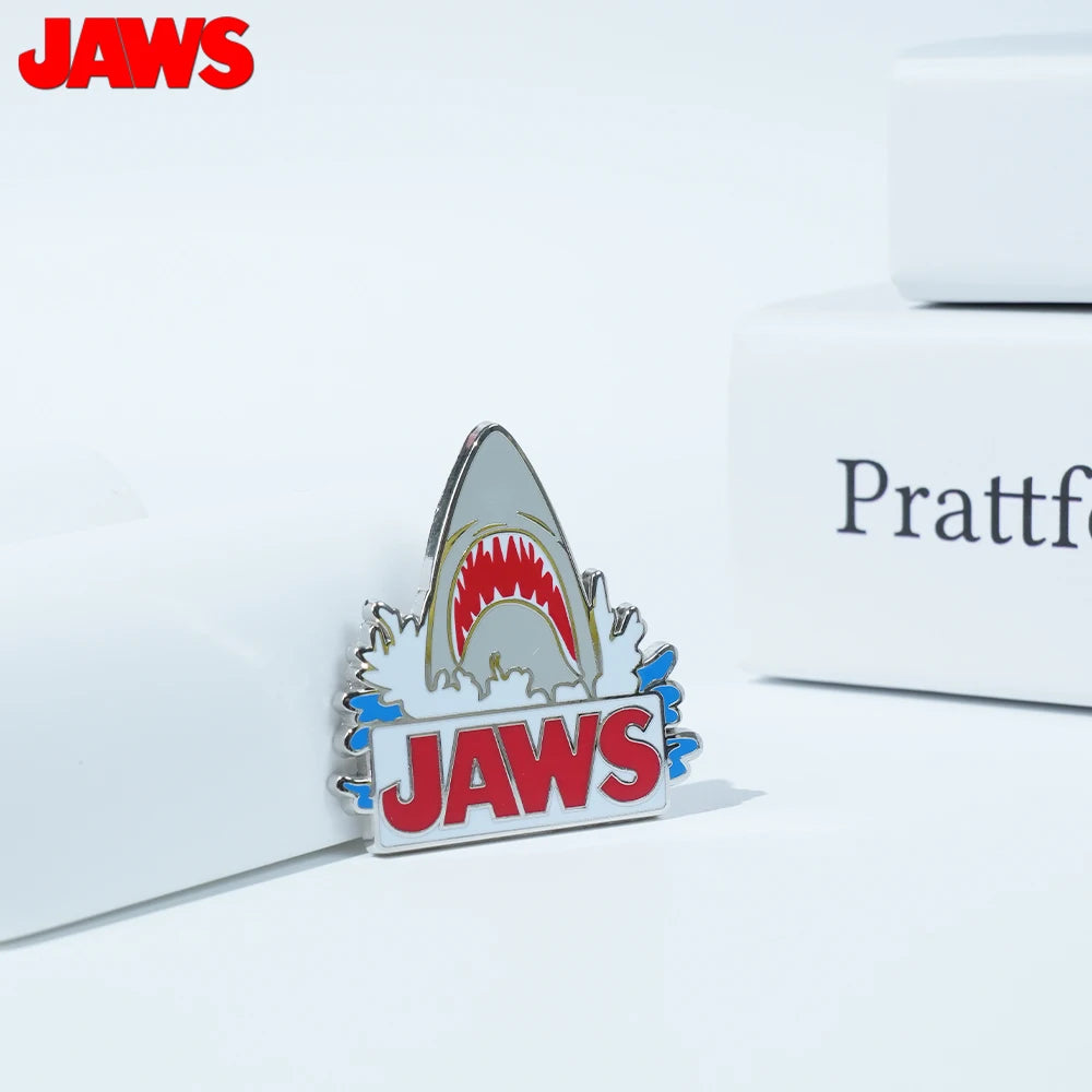 Silver enamel lapel pin featuring a shark tooth design and the word JAWS