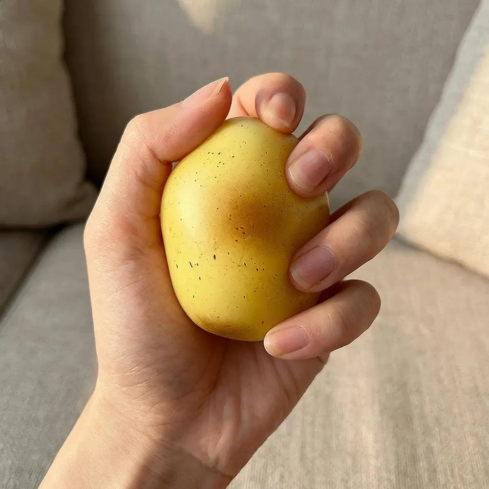 A hand is holding a yellow fluid potato squishy toy against a soft, light-colored background.
