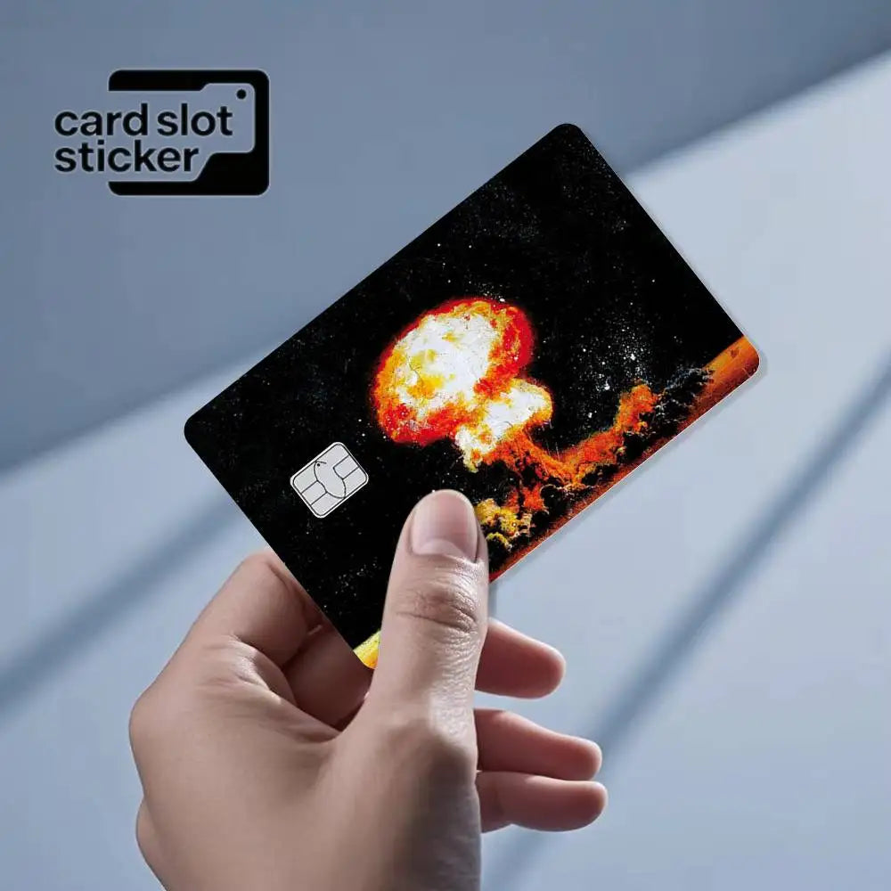 A hand holds a black card sticker featuring a bright orange and yellow explosion against a dark starry background.