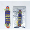 A finger skateboard is shown, packaged in a clear plastic bag with a purple and yellow design.
