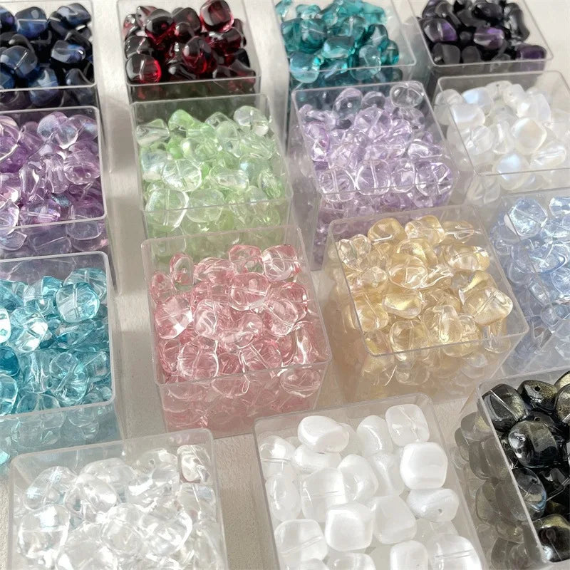 Assortment of geometric glass beads in various colors including purple, green, pink, and clear shades for jewelry making