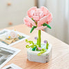 A pink rose flower building block bouquet set with green stems and leaves on a wooden table.