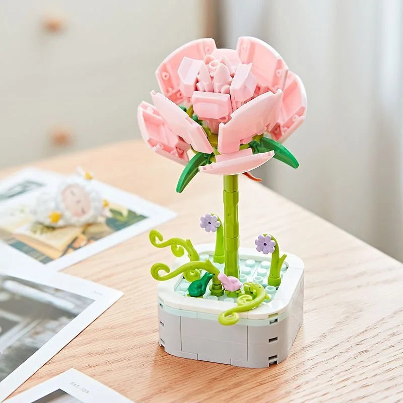 A pink rose flower building block bouquet set with green stems and leaves on a wooden table.