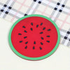 A red watermelon shaped PVC coaster with black seeds rests on a checkered cloth.