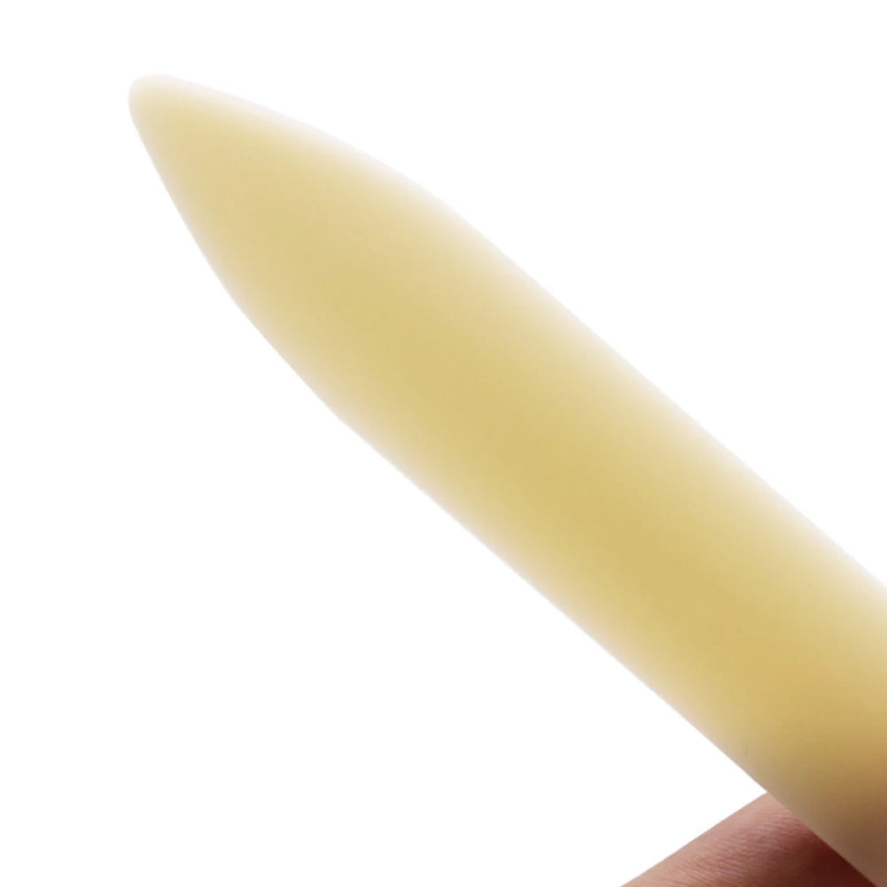 A close-up view of a pale yellow plastic bone folder used for paper creasing and folding crafts.