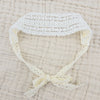 White floral lace baby headband with a gathered bow on a beige textured fabric.