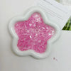A white flower-shaped mold filled with pink glitter acrylic filler for nail art and DIY crafts