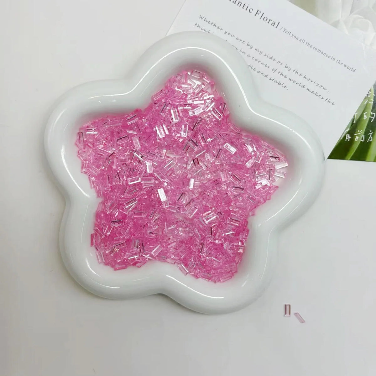 A white flower-shaped mold filled with pink glitter acrylic filler for nail art and DIY crafts