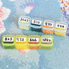 A collection of small plastic storage boxes filled with colored beads or sequins, arranged in a row on a light blue patterned