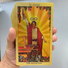 A golden foil tarot card titled El Mago featuring a figure holding a wand and surrounded by light.