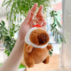 A hand holds an adorable brown capybara plush keychain charm with a white collar and gold ring.