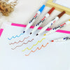 A set of six white paint pens with colored tips are arranged on a white sheet of paper.