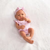 A lifelike vinyl reborn doll with a pink bow and striped outfit lying on white fluffy material.
