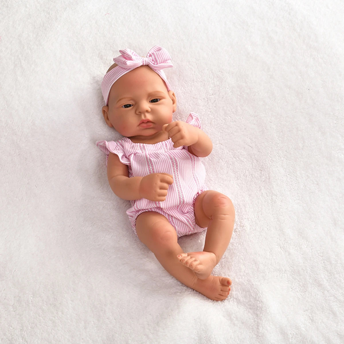 A lifelike vinyl reborn doll with a pink bow and striped outfit lying on white fluffy material.