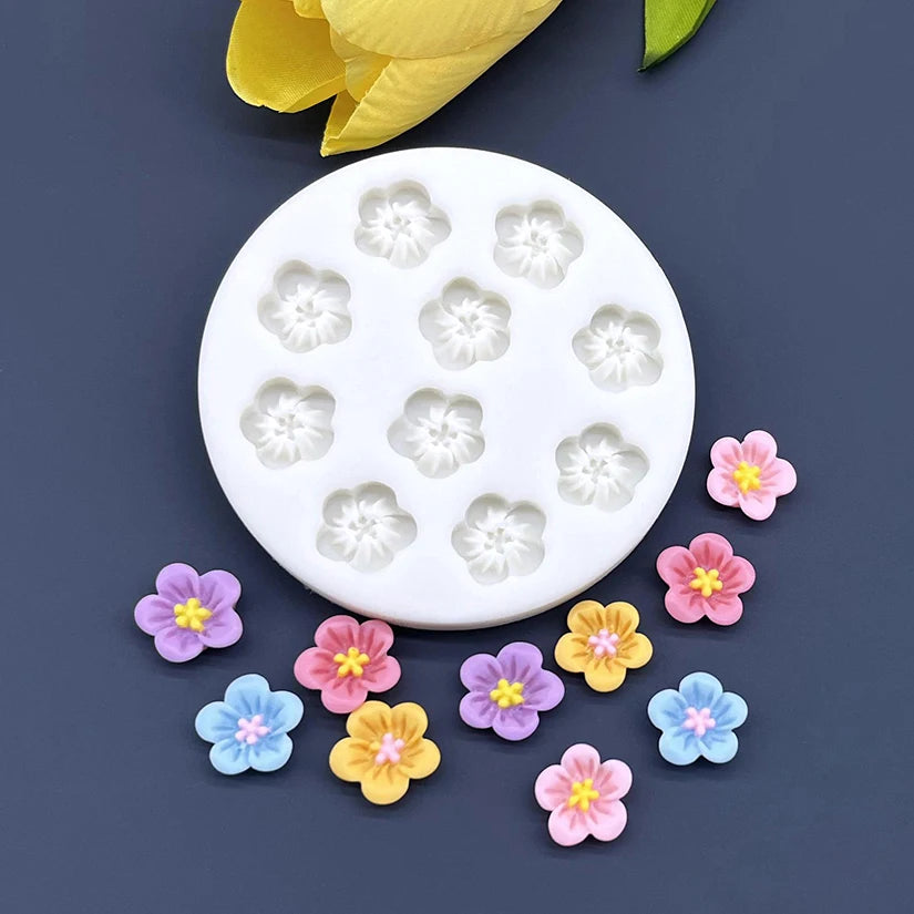 White silicone mold with small flower shapes and several colorful fondant flowers scattered below.