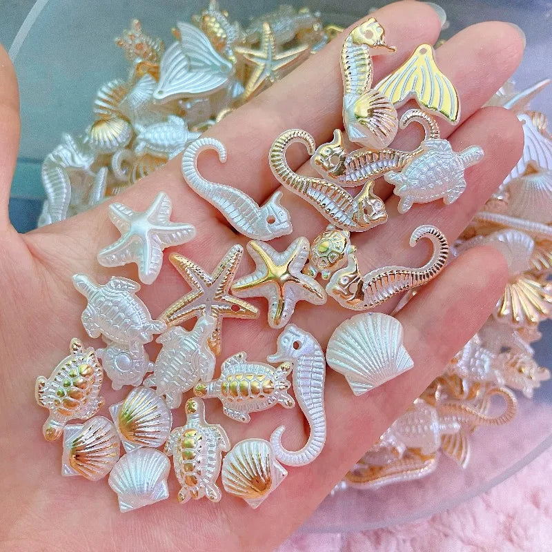 A hand holds a collection of white and gold acrylic ocean animal beads for DIY jewelry making.