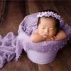A newborn baby is sleeping inside a purple knit wrap with a lilac pearl headband.