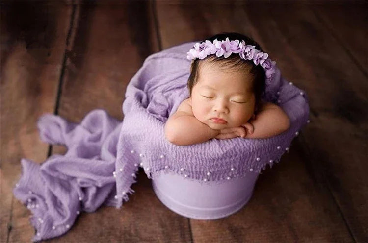 A newborn baby is sleeping inside a purple knit wrap with a lilac pearl headband.