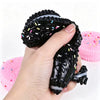 A hand holds a black biscuit squishy stress relief toy with pink sprinkles and a pink version.