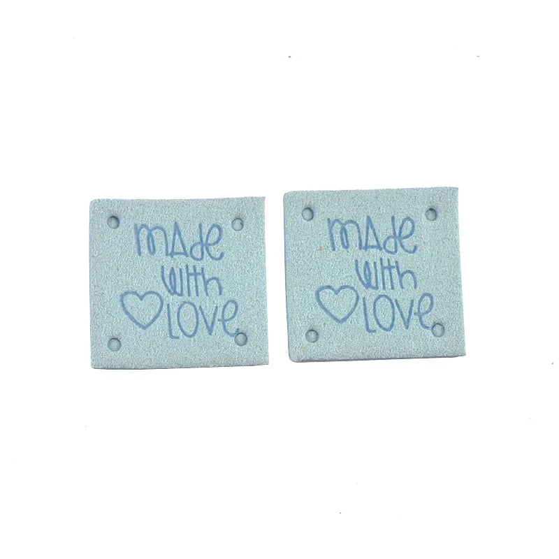 A set of two light blue embossed leather labels for sewing and crafts, each engraved with Made with love.