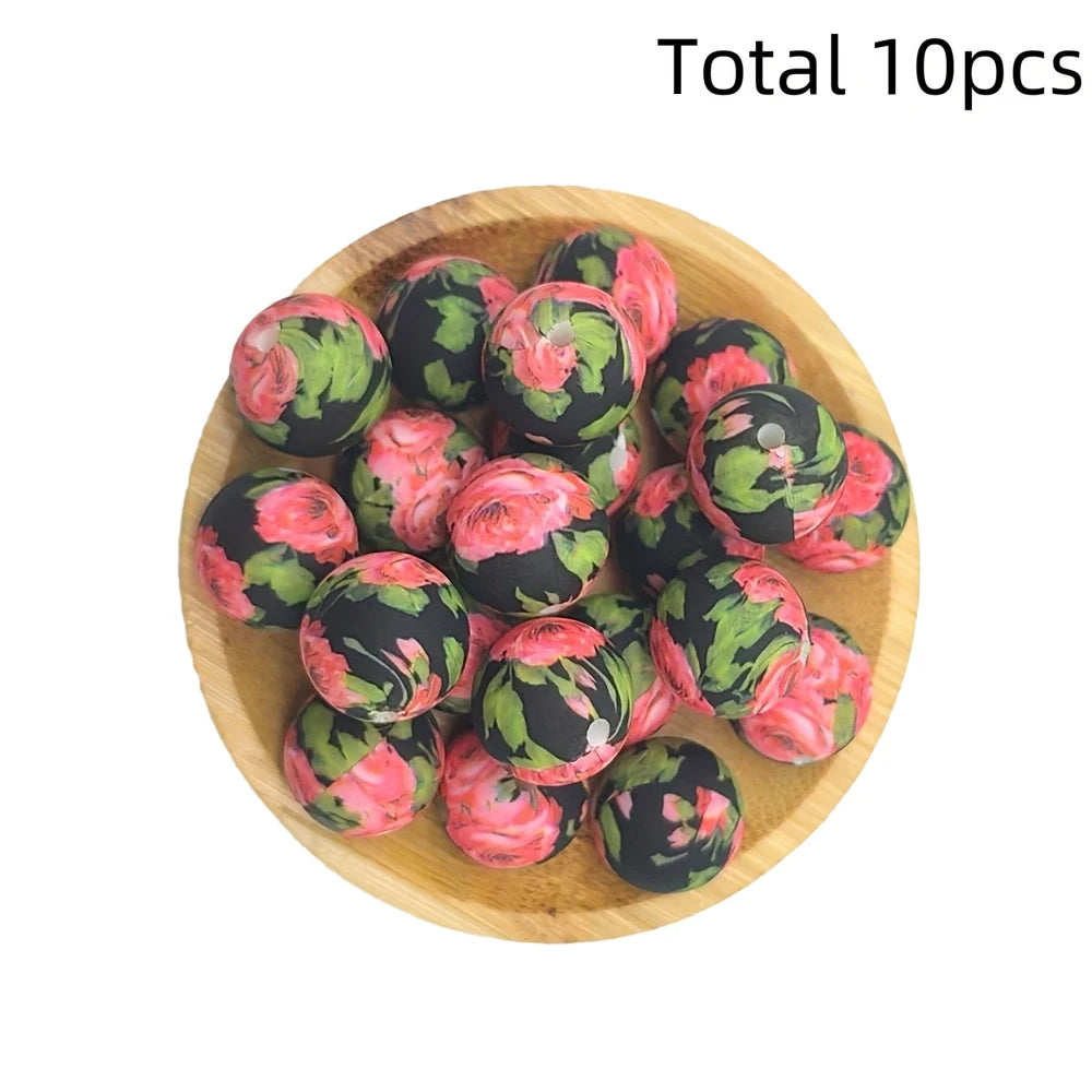 A wooden bowl filled with ten pink and green floral printed silicone beads for DIY jewelry making